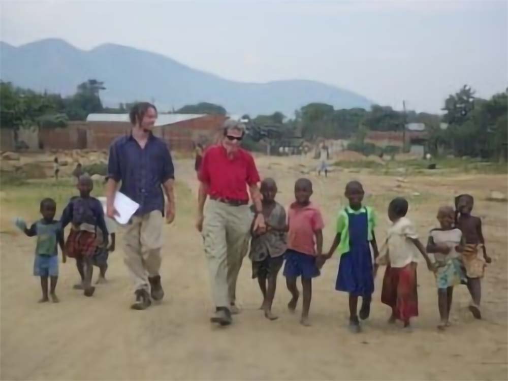 Kasese and another man walking with small children from an African village with a mountain in the background